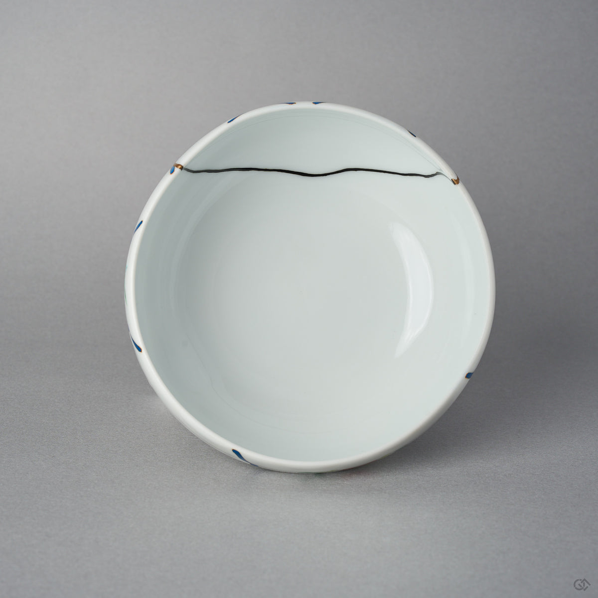 Top view of the Arita lidded bowl body without its lid, white porcelain interior with a fine black urushi restoration line crossing near the rim between blue urushi marks.