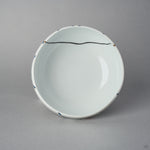 Top view of the Arita lidded bowl body without its lid, white porcelain interior with a fine black urushi restoration line crossing near the rim between blue urushi marks.