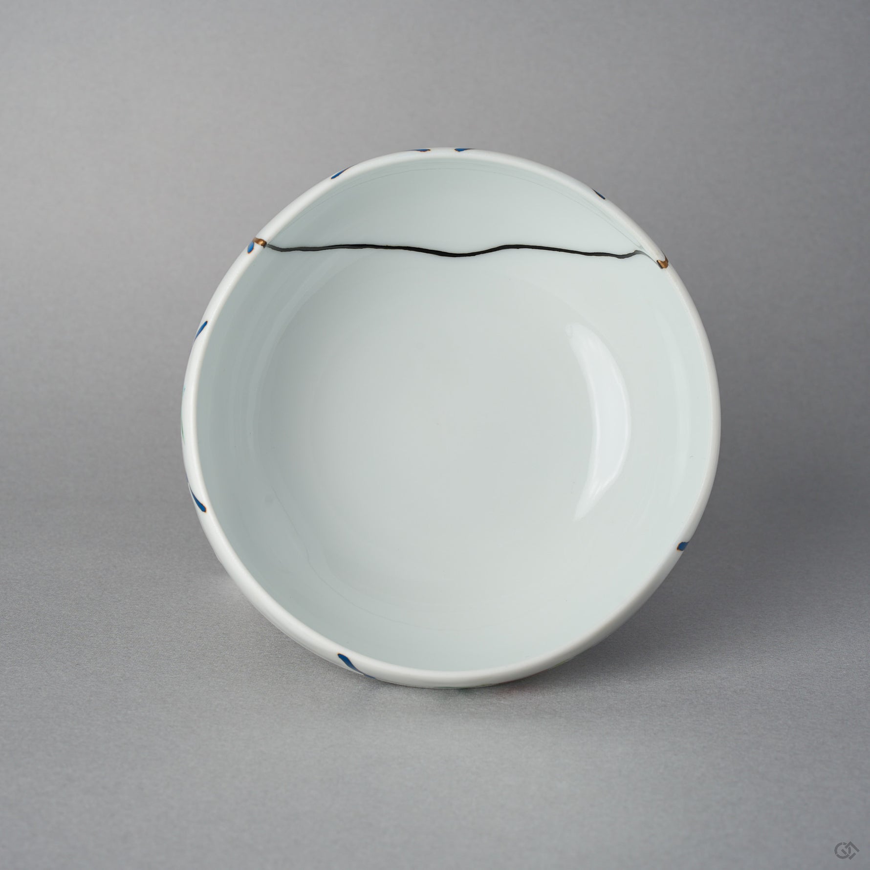 Top view of the Arita lidded bowl body without its lid, white porcelain interior with a fine black urushi restoration line crossing near the rim between blue urushi marks.
