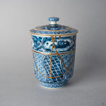 Kintsugi lidded tea cup in Kyoto ware: urushi and 24K gold seams cross the blue shonzui panels and sansui band, the intact gilt lid in place, front view.