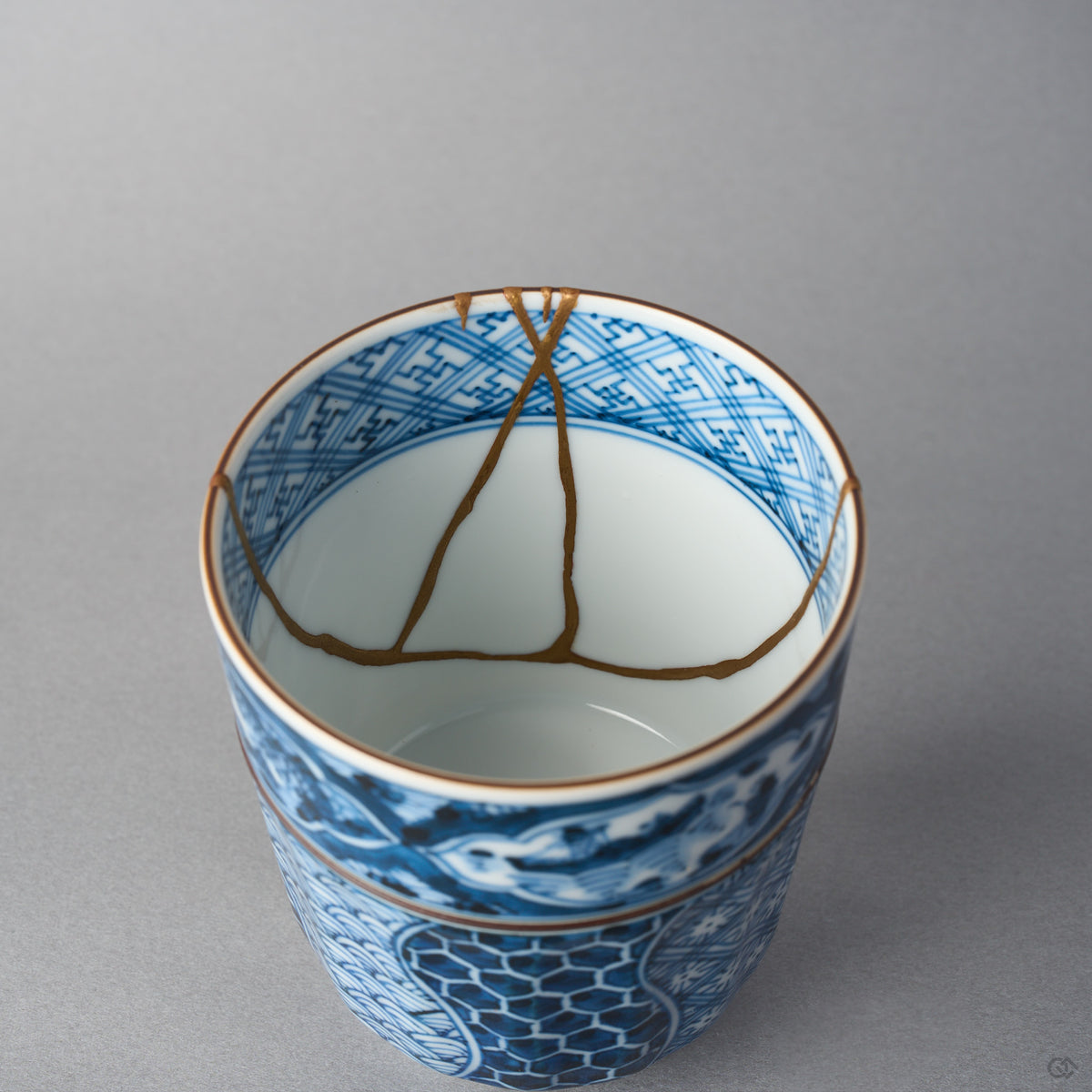 Kintsugi tea cup interior where gold urushi seams descend the deep white wall and converge near the center of the bowl.