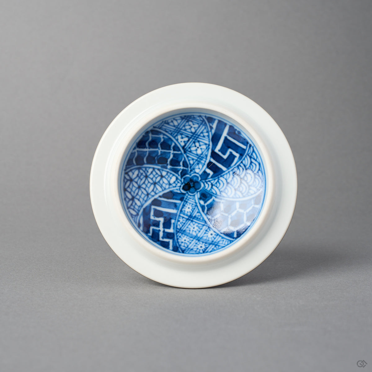 Underside of the intact lid of the kintsugi lidded tea cup, showing the pinwheel inner well and blue border; no restoration is visible in this view.