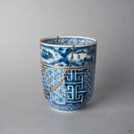 Kintsugi tea cup side view: a gold urushi line follows the painted landscape band and a V-shaped 24K gold seam crosses the shonzui body.