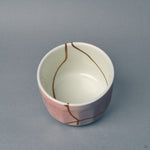 Inside the white porcelain bowl, gold kintsugi lines descend from the rim — a story in every seam against a mirror glaze.