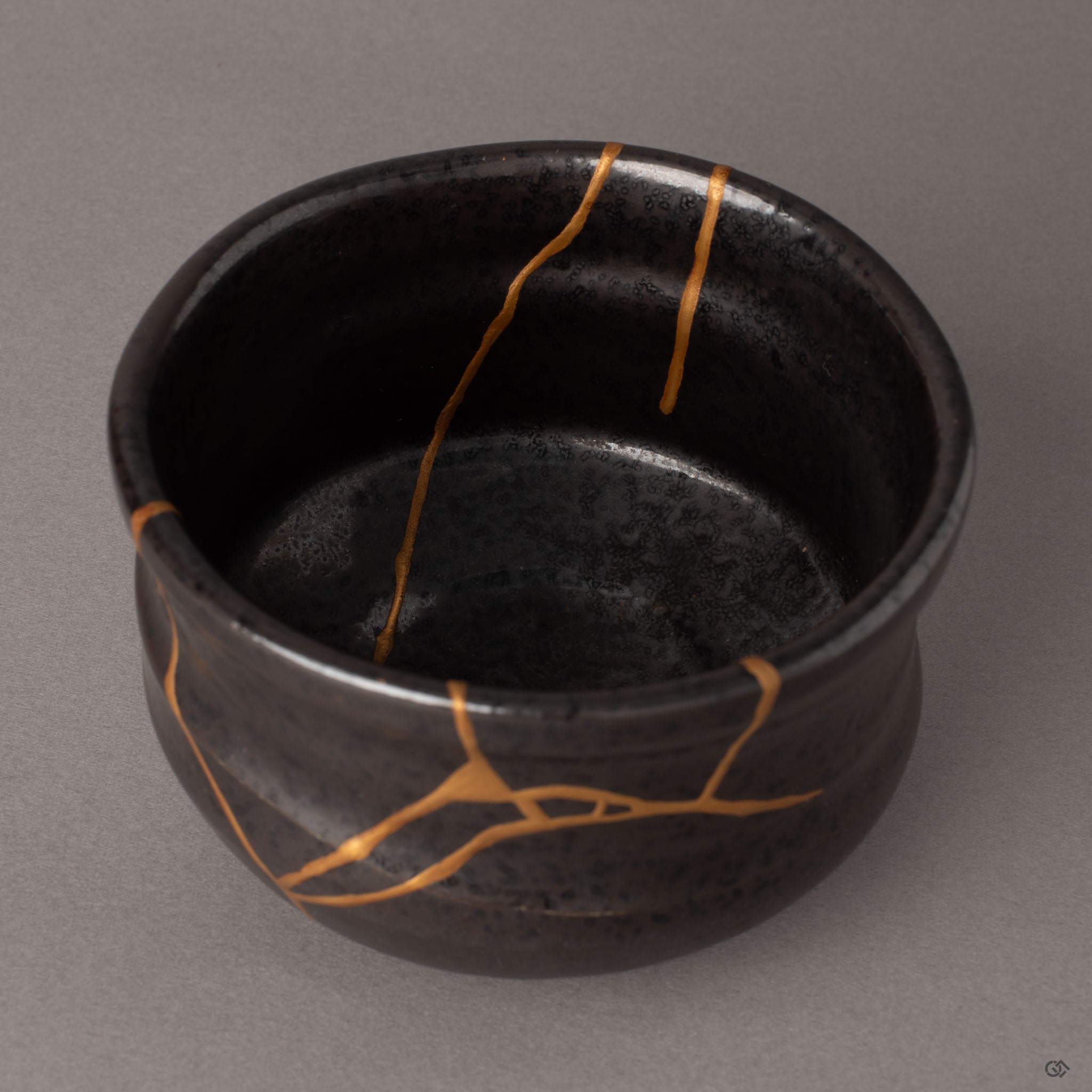 Gold kintsugi seams crossing the dark interior of an Arita porcelain matcha bowl, each fracture path carrying restorative beauty.