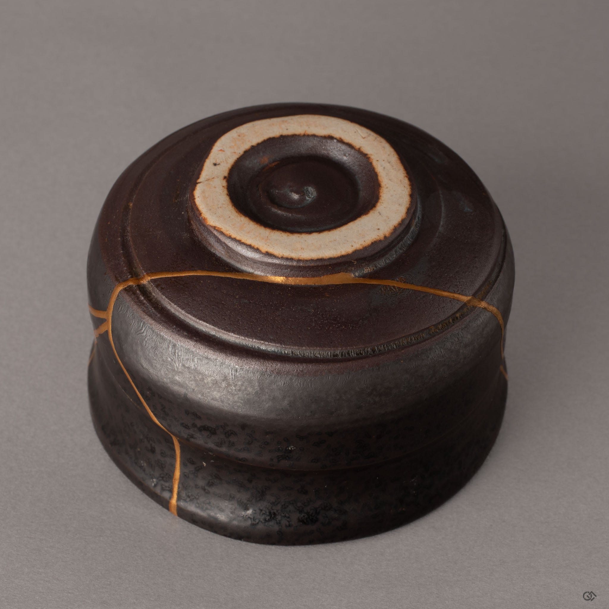 Lower section of a kintsugi Arita matcha bowl where gold restoration lines reach toward the unglazed foot, history made visible in clay.