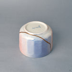 From the side, the bowl's rounded form turns toward its blue field, where a gold kintsugi line marks beauty in imperfection.