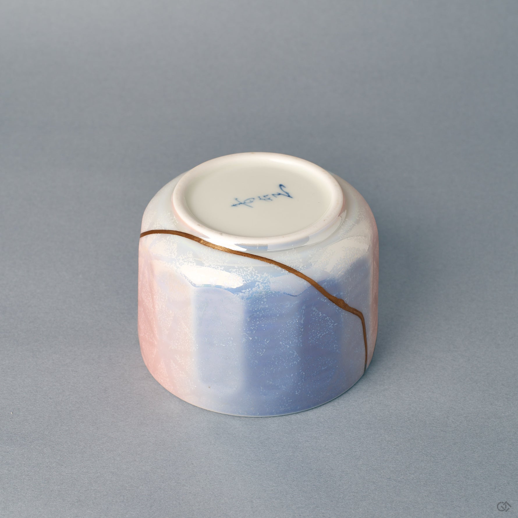 From the side, the bowl's rounded form turns toward its blue field, where a gold kintsugi line marks beauty in imperfection.