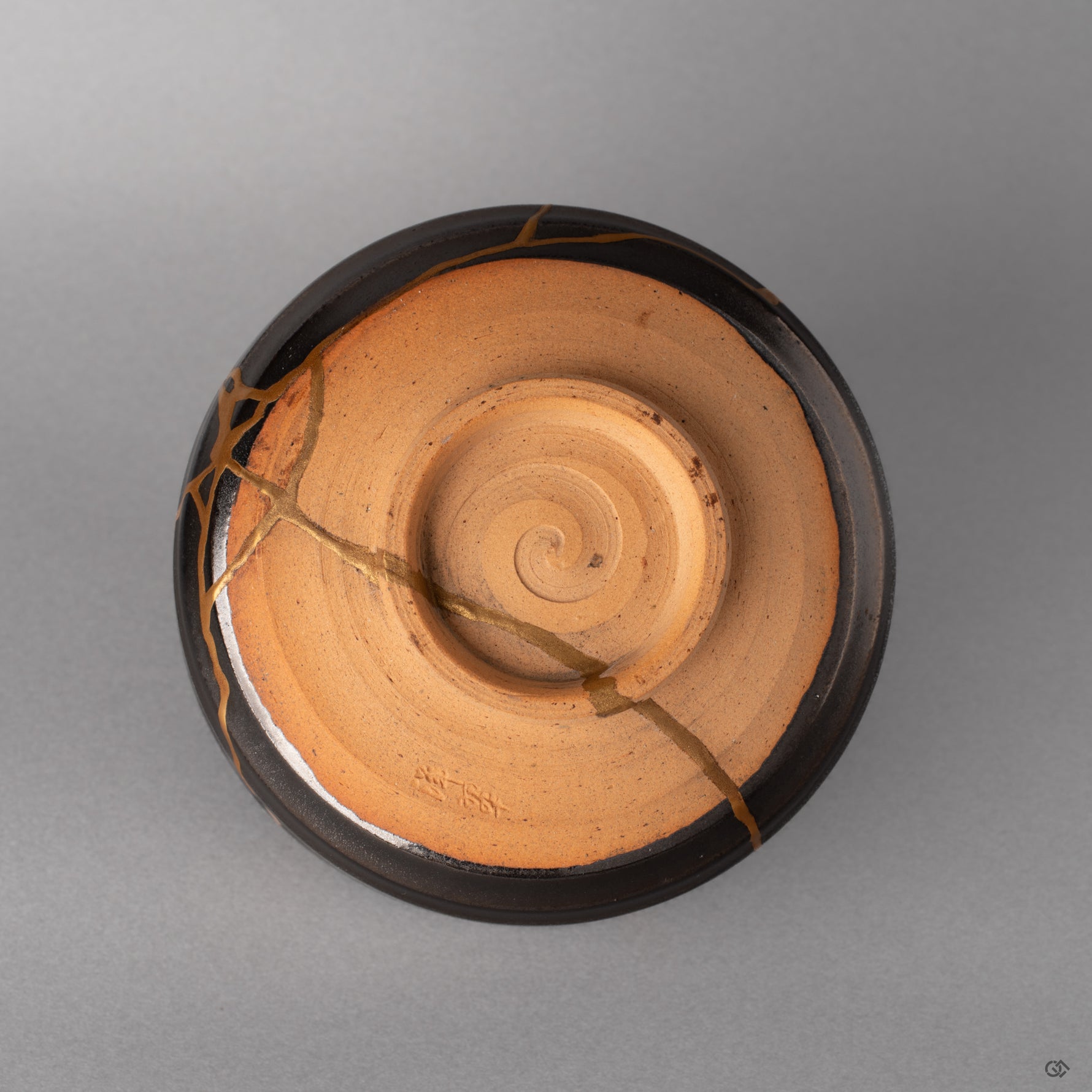The foot ring of this Arita kintsugi bowl grounds the piece, dark glaze meeting bare clay, history made visible at the base.