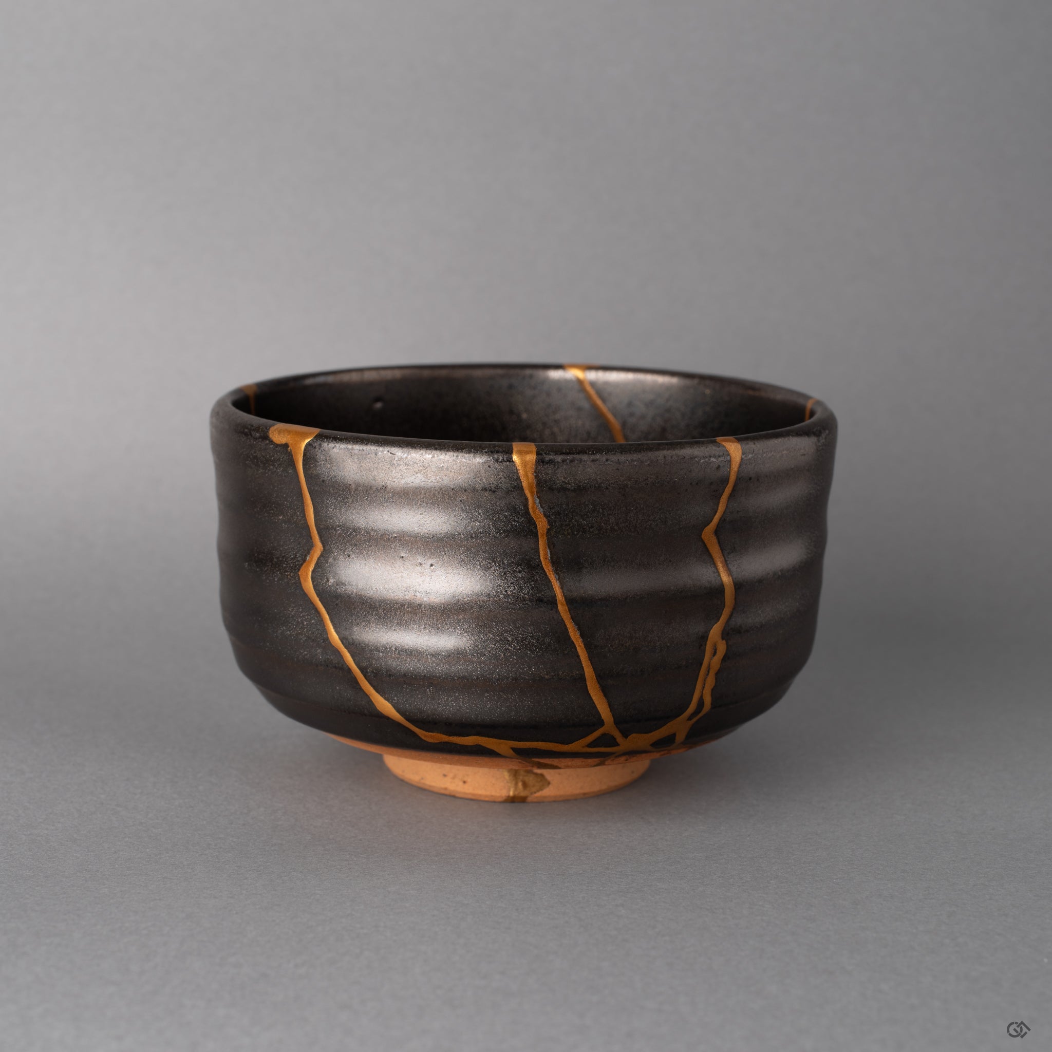 Dark gray Arita matcha bowl with bold kintsugi lines in 24K gold crossing its minimalist surface, wabi-sabi in restrained form.