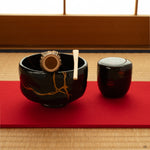 Kintsugi black matcha bowl on tatami in natural light, restored with gold and resting in a moment of contemplation.