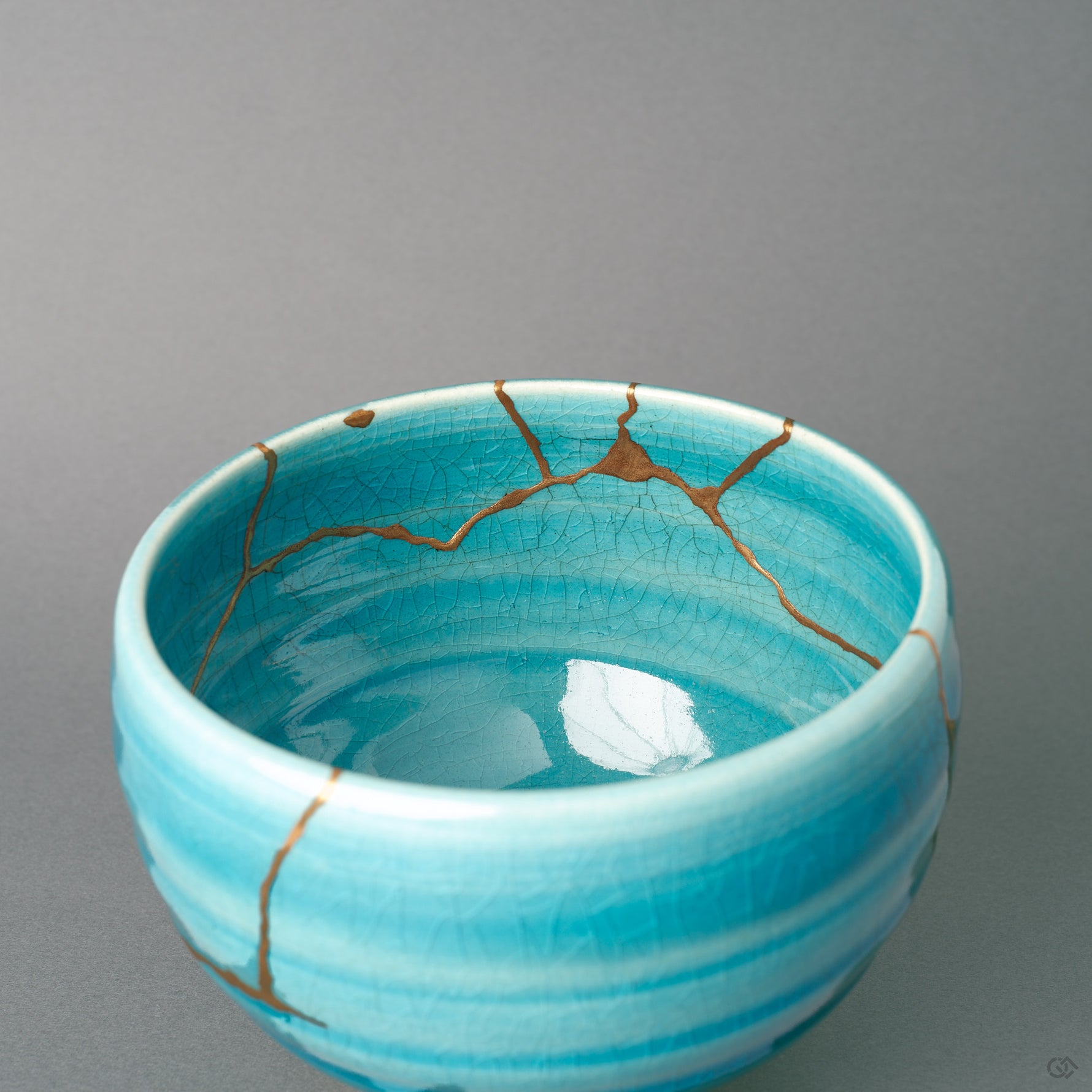 Inside the kintsugi bowl, a fine gold line reaches the rim above the crackled turquoise glaze, slow craft seen up close.