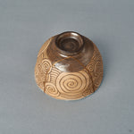 Side view of a kintsugi matcha bowl where incised spirals wrap the warm earthenware body, a quiet beauty held in clay.