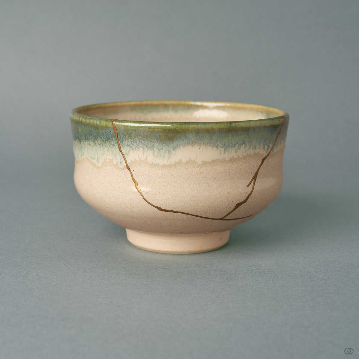 From the side, this kintsugi matcha bowl shows a green-to-blue glaze band wrapping a rounded earthenware form, history made visible in gold.