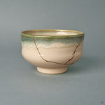 From the side, this kintsugi matcha bowl shows a green-to-blue glaze band wrapping a rounded earthenware form, history made visible in gold.