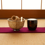 The kintsugi bowl rests on tatami in soft light, its gold seam catching a moment of contemplation.