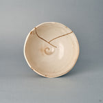 Seen from above, the kintsugi bowl's round mouth frames a cream interior, its carved spirals one-of-a-kind.