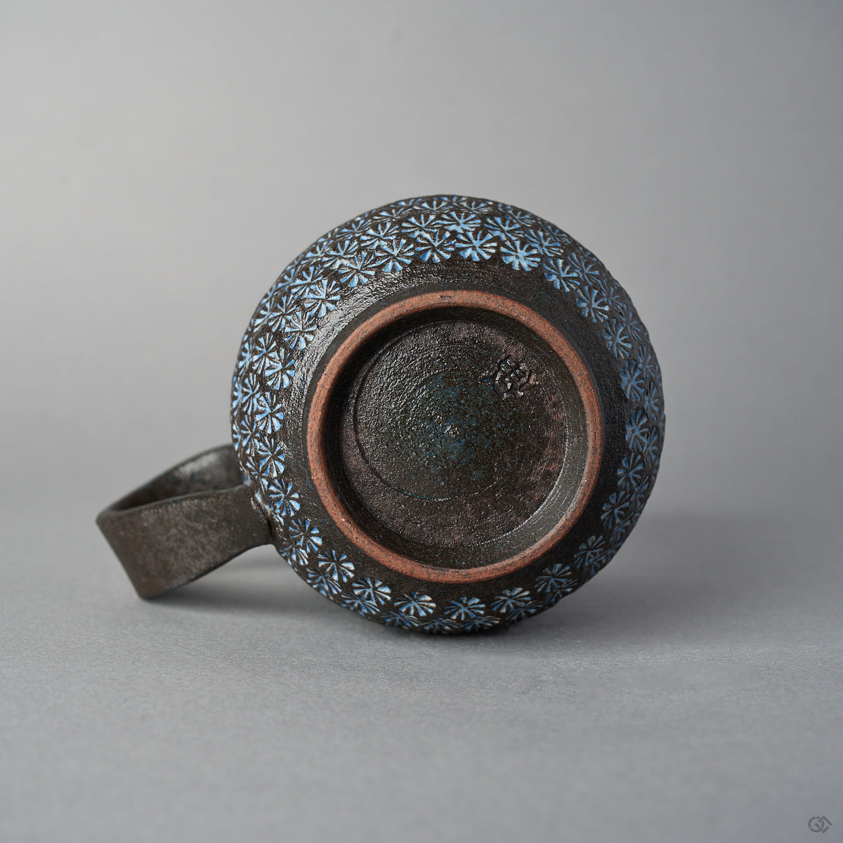 Underside of the Kyoto ware mug showing the unglazed foot ring, dark fired clay with a stamped potter's mark, and white mishima florets circling the body.