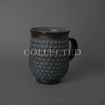 Kyoto ware kintsugi mug in dark clay stamped with white mishima florets, its rim restored in 24K gold above a rising sun painted in urushi-e on the inner wall. Collected.