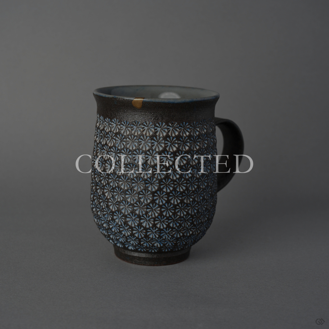 Kyoto ware kintsugi mug in dark clay stamped with white mishima florets, its rim restored in 24K gold above a rising sun painted in urushi-e on the inner wall. Collected.