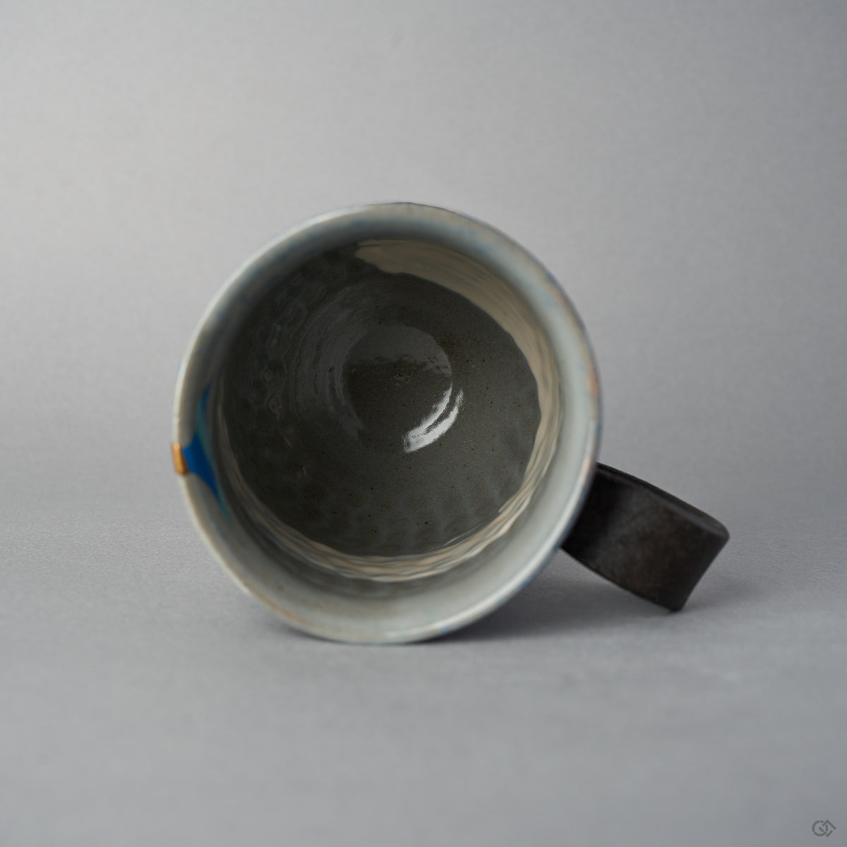 Top view into the Kyoto ware kintsugi mug, grey-blue glazed interior with the blue urushi-e sun and the 24K gold rim restoration visible at the edge.