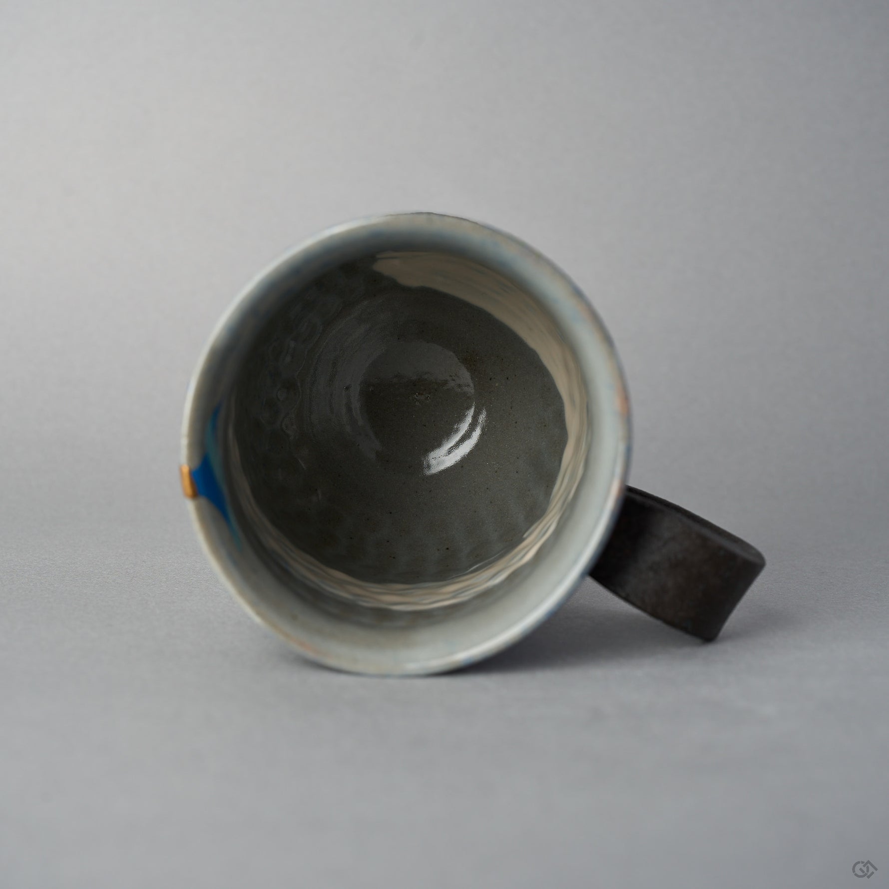 Top view into the Kyoto ware kintsugi mug, grey-blue glazed interior with the blue urushi-e sun and the 24K gold rim restoration visible at the edge.