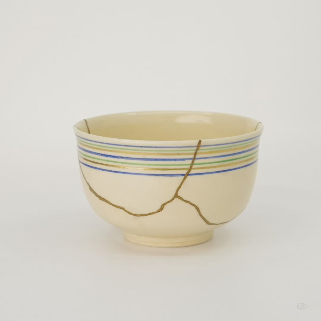 Rotation video of the Kyoto ware kintsugi cup in cream earthenware, turning to show the koma-suji rim lines and the network of 24K gold seams around the body.