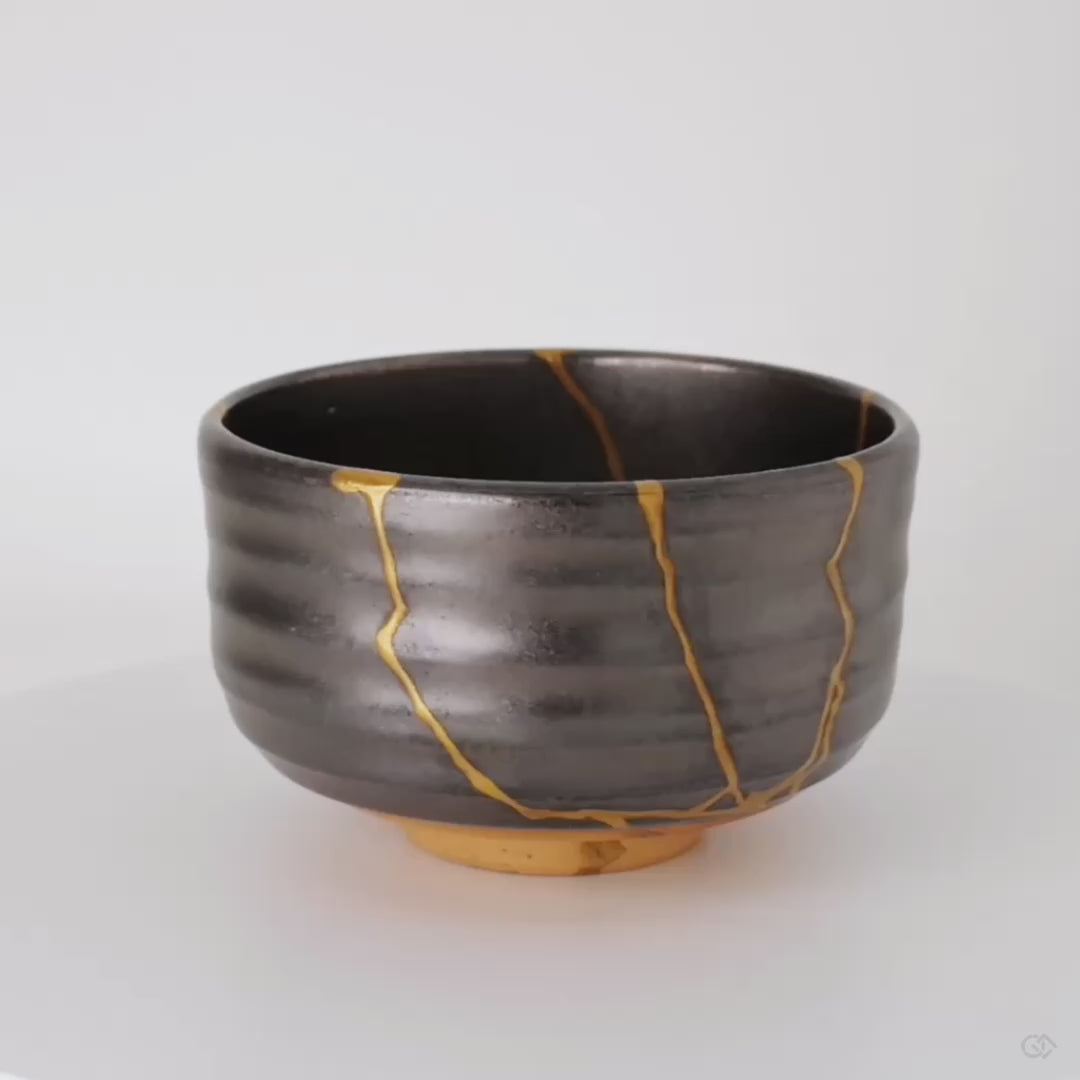 The dark Arita matcha bowl turns slowly, kintsugi seams in 24K gold appearing from every angle, visible resilience in motion.