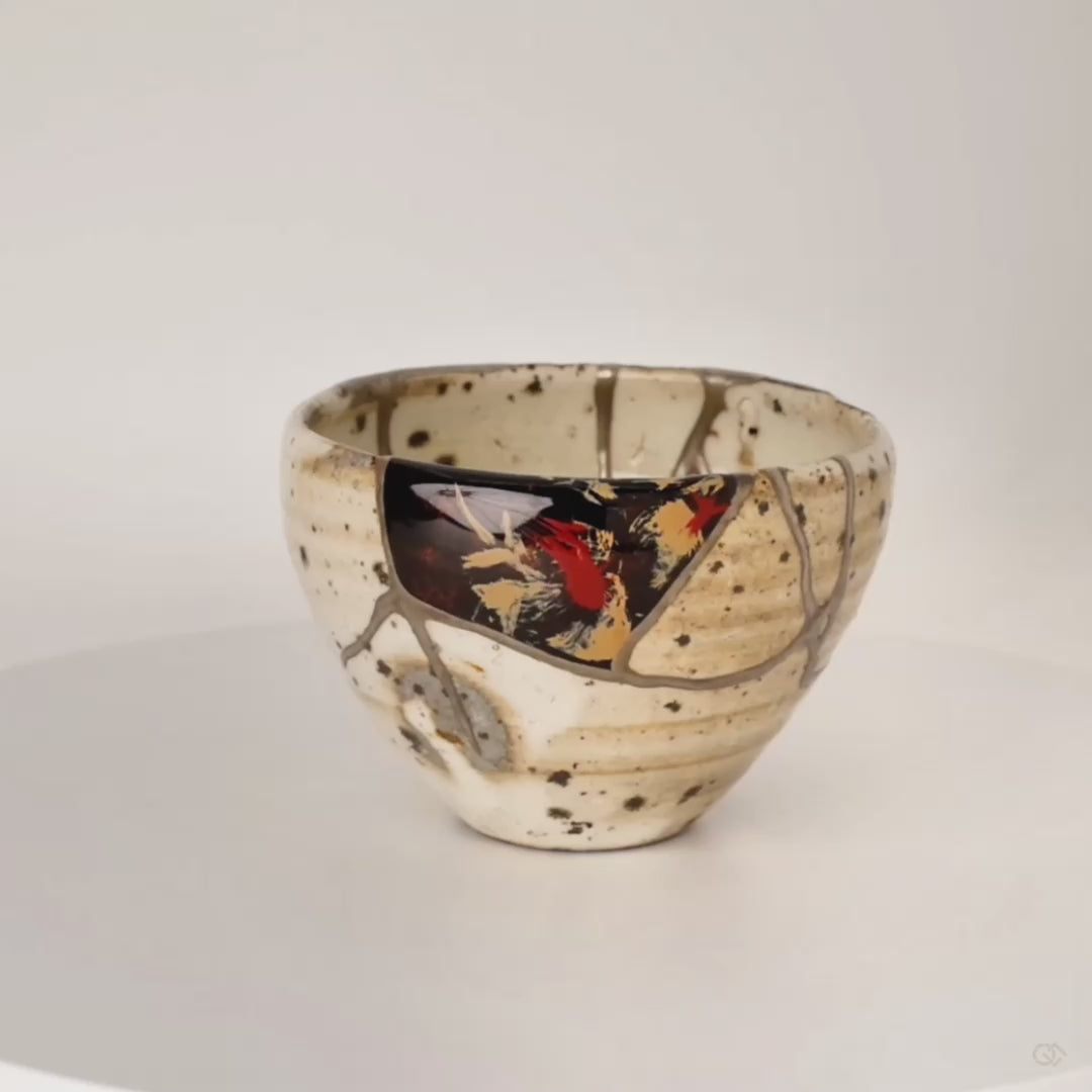 Slow 360-degree rotation of a kintsugi Shigaraki cup, silver seams and urushi-e lacquer painting revealed from every angle as the vessel turns, enduring legacy in motion.