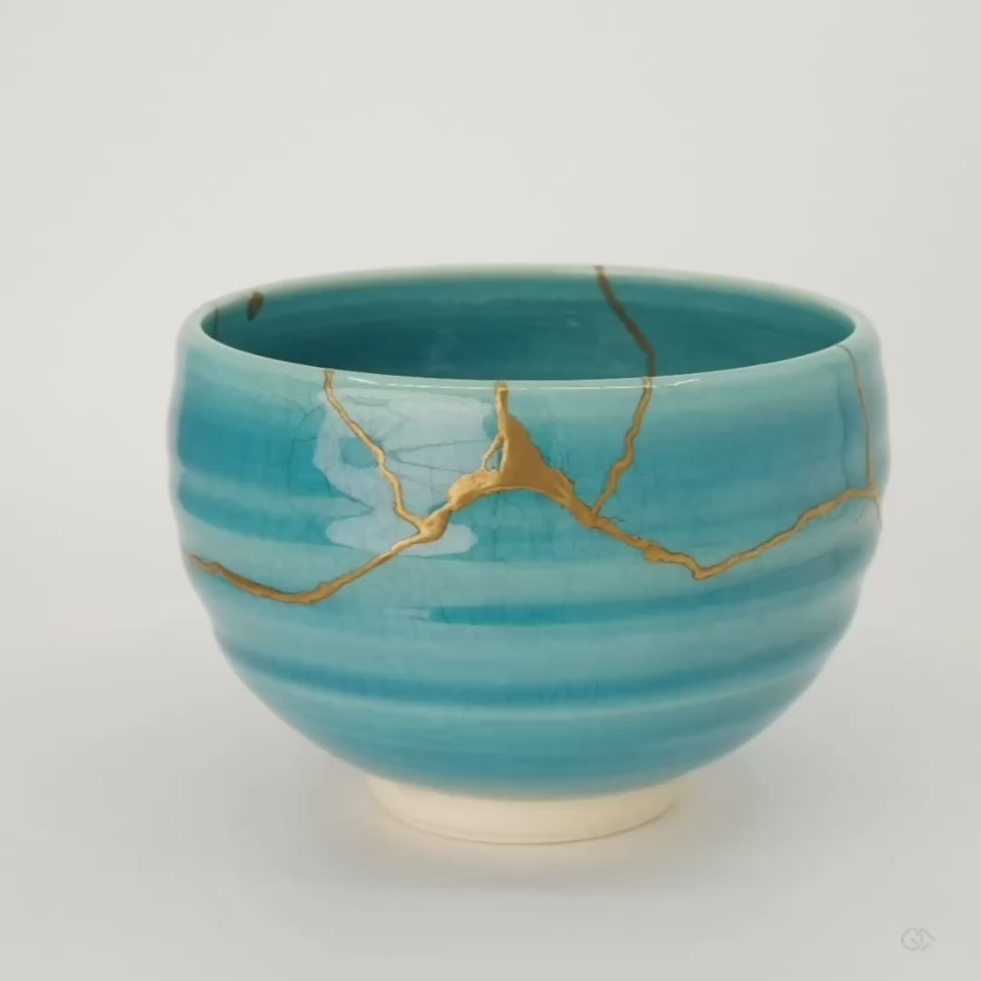 A 360-degree turn of the kintsugi Kyoto bowl, gold seams catching light across the turquoise glaze, museum-worthy craftsmanship in motion.