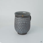 Rotating view of a Kyoto ware mug in dark stamped clay with white mishima florets and 24K gold kintsugi at the rim, turning to show the full restoration.