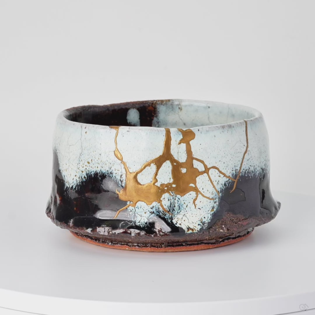 Rotating view of a Karatsu ware matcha bowl in white and black glaze with natural urushi and 24K gold kintsugi seams, turning to show the full restoration.