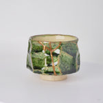 Rotating view of a kintsugi sake cup in faceted Oribe green pottery with natural urushi and 24K gold seams, turning to show the full restoration.