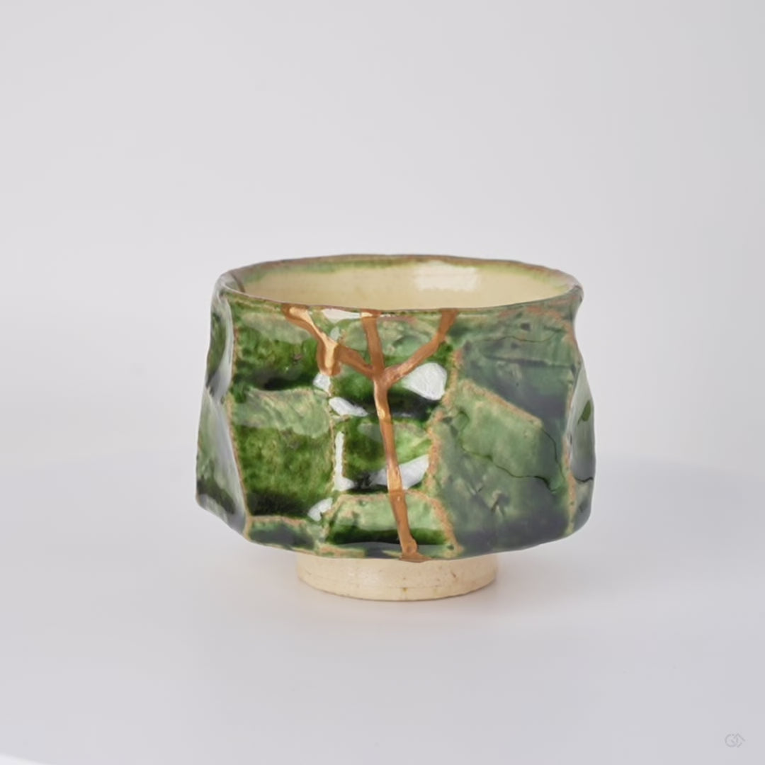 Rotating view of a kintsugi sake cup in faceted Oribe green pottery with natural urushi and 24K gold seams, turning to show the full restoration.