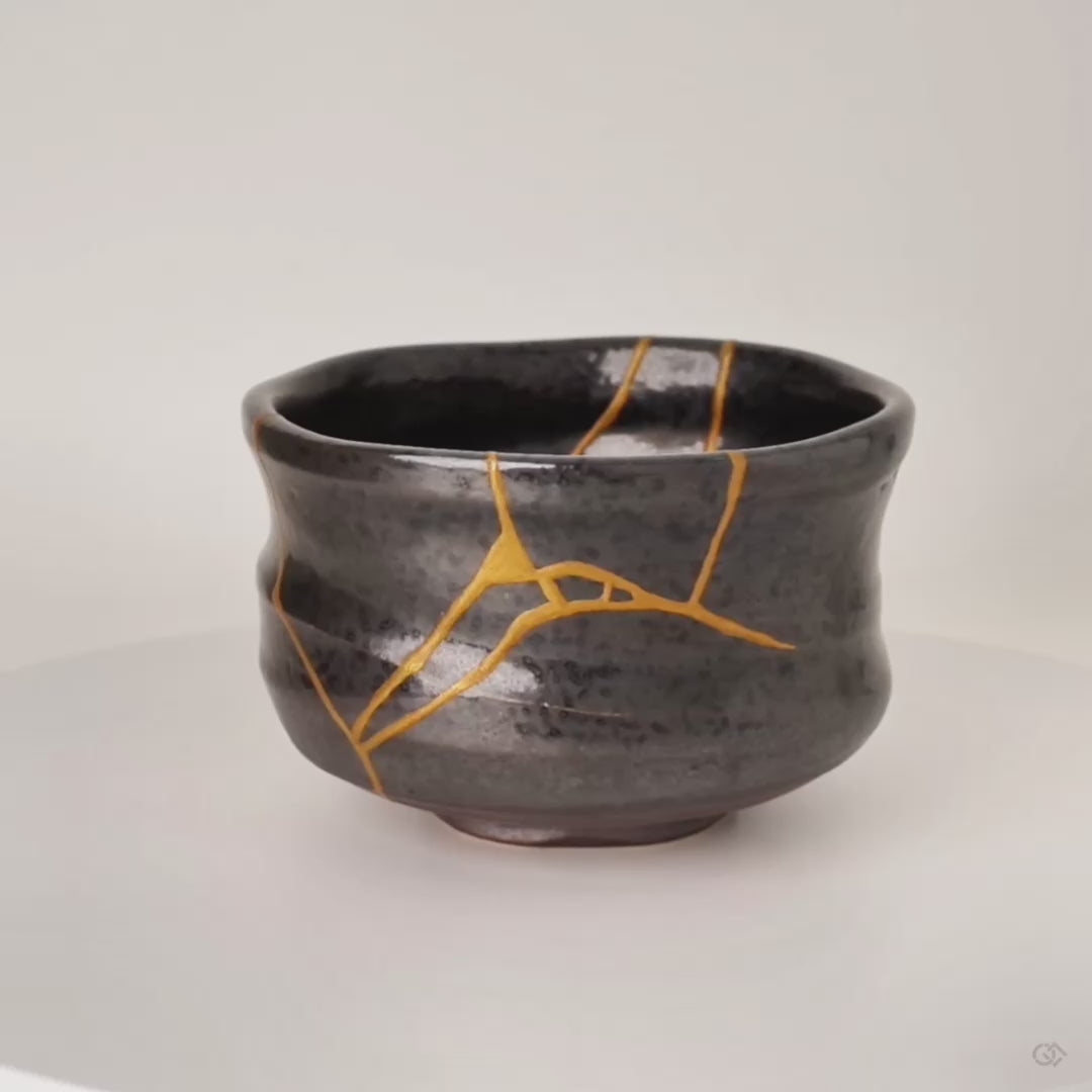 360-degree rotation of a kintsugi Arita matcha bowl, gold seams turning slowly across dark porcelain, revealing an enduring legacy.