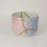A 360-degree turn of the kintsugi Arita bowl, gold seams moving across the rose-and-blue glaze — urushi as a living philosophy.