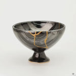Rotating view of an Arita ware footed bowl in black porcelain with 24K gold kintsugi seams, turning to show the striped glaze and the full restoration around the vessel.
