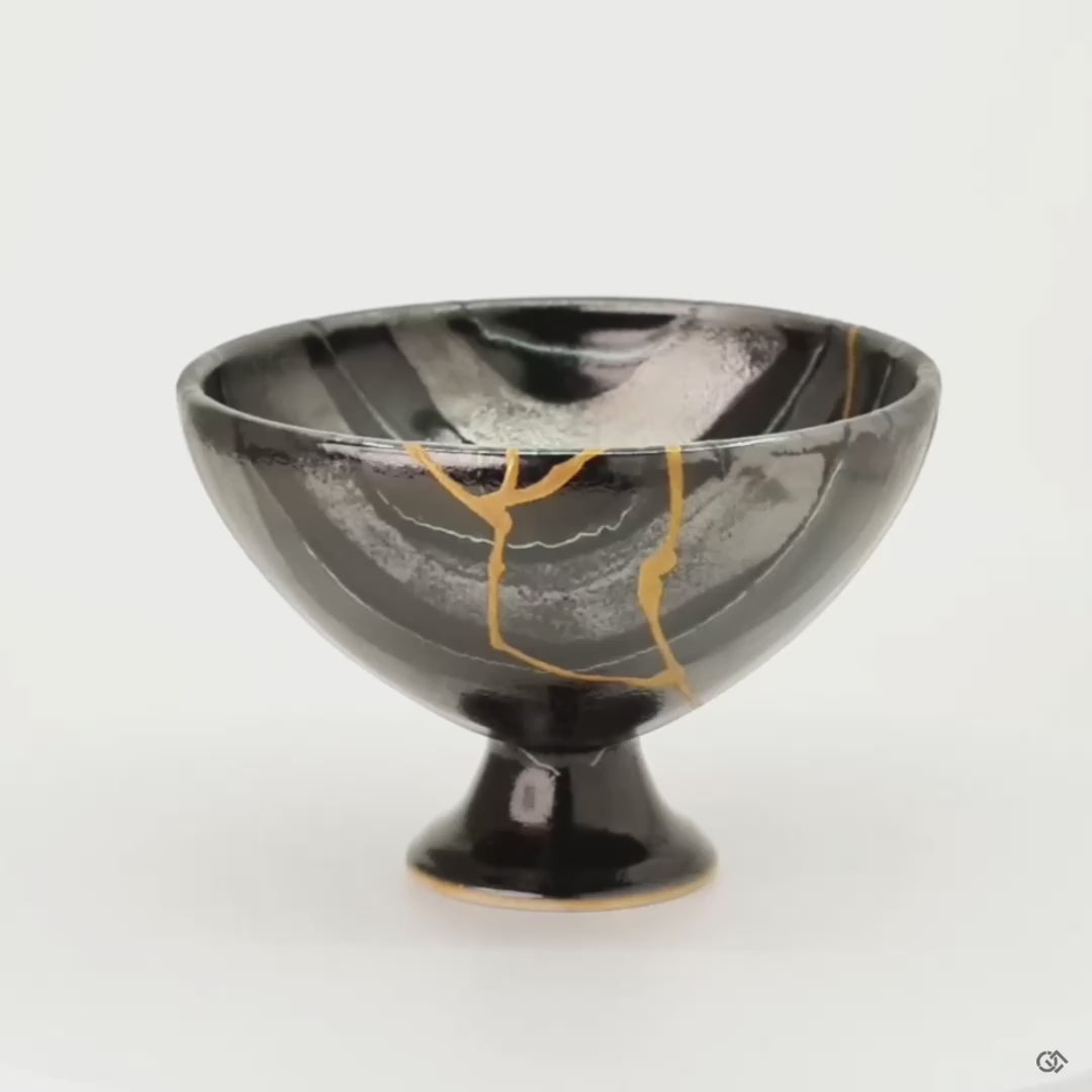 Rotating view of an Arita ware footed bowl in black porcelain with 24K gold kintsugi seams, turning to show the striped glaze and the full restoration around the vessel.
