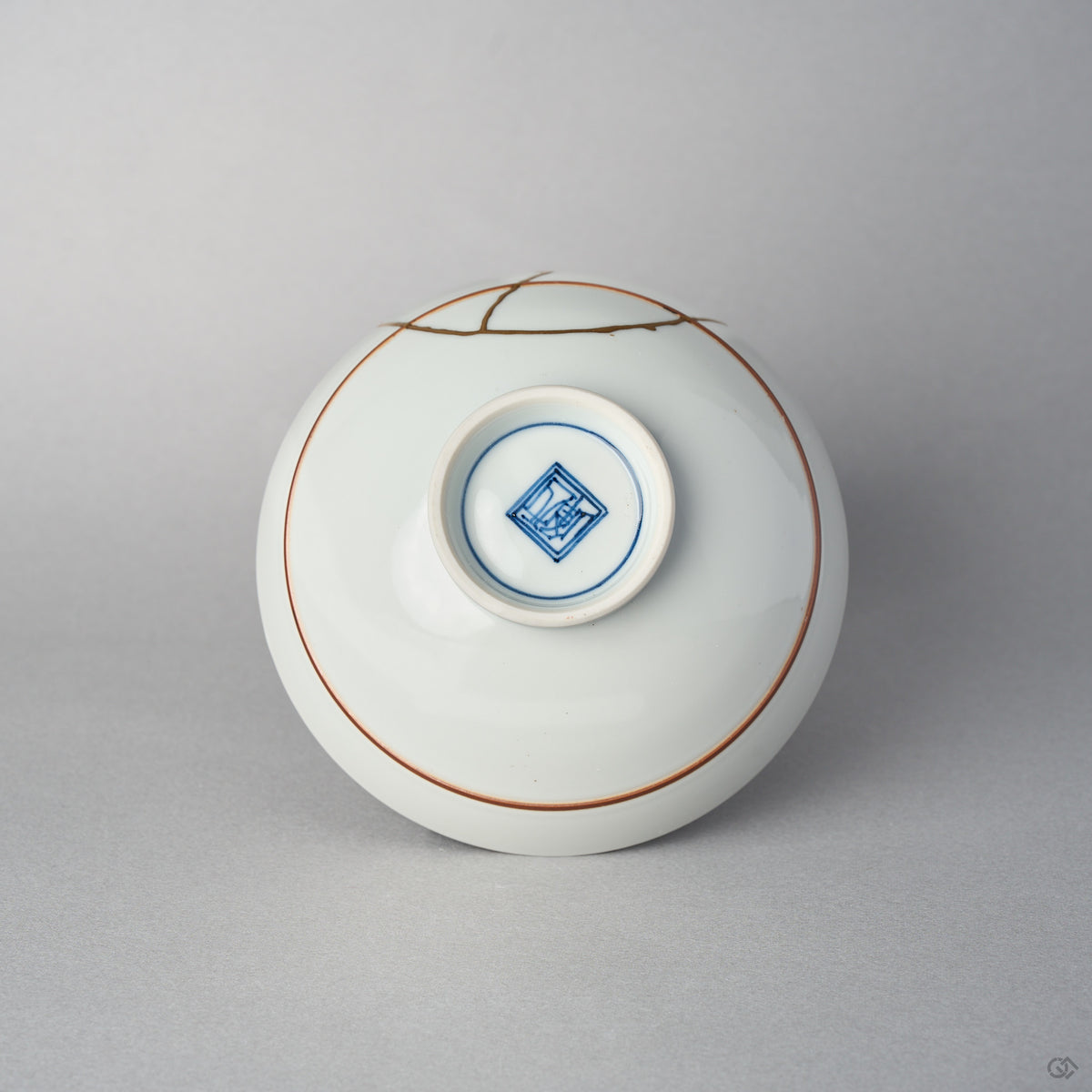 Underside of a Kyoto ware porcelain rice bowl with a painted mark inside the footring, the 24K gold kintsugi seam reaching over the white glazed base.
