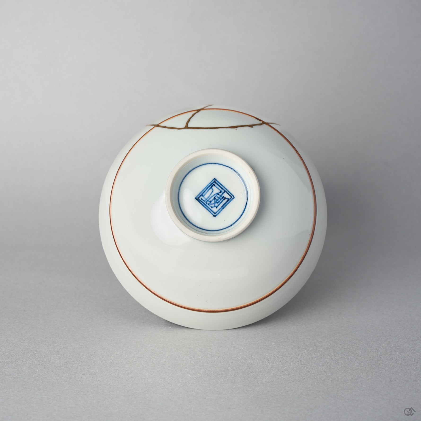 Underside of a Kyoto ware porcelain rice bowl with a painted mark inside the footring, the 24K gold kintsugi seam reaching over the white glazed base.