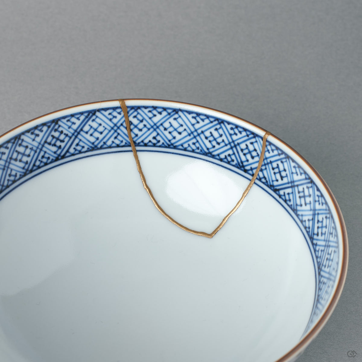 Inside the kintsugi rice bowl, a blue lattice pattern rings the well while a gold seam crosses the rim — tactile history within reach.