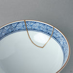 Inside the kintsugi rice bowl, a blue lattice pattern rings the well while a gold seam crosses the rim — tactile history within reach.