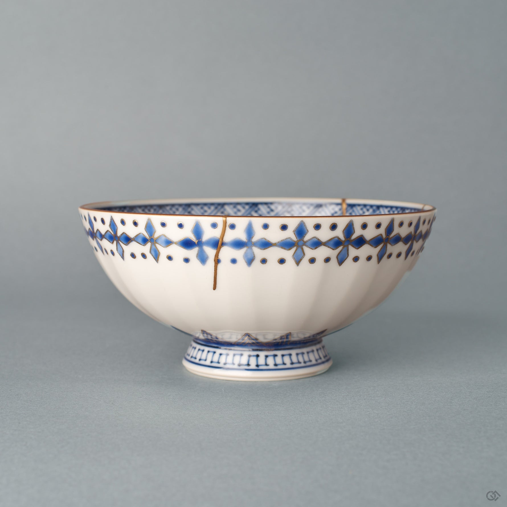 Side profile of the kintsugi rice bowl, gold lines descending from the rim toward the key-fret foot — history made visible across the curve.