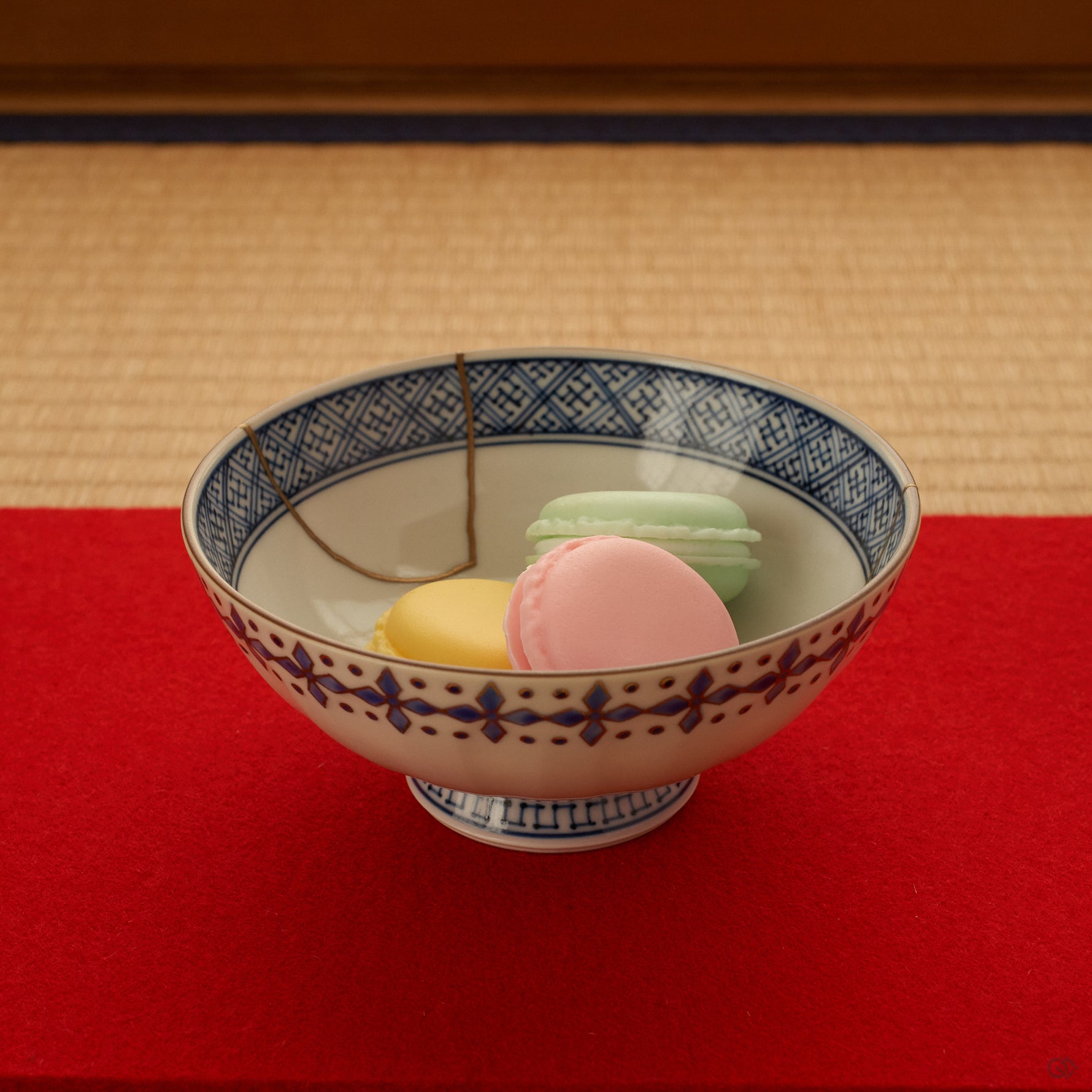 The kintsugi rice bowl rests on tatami in soft daylight, its gold seams and sometsuke blue quiet against the woven mat, conscious luxury at the table.