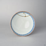 Top view of a kintsugi Kyoto ware rice bowl, the cobalt lattice border encircling a white porcelain well crossed by a branching 24K gold seam.
