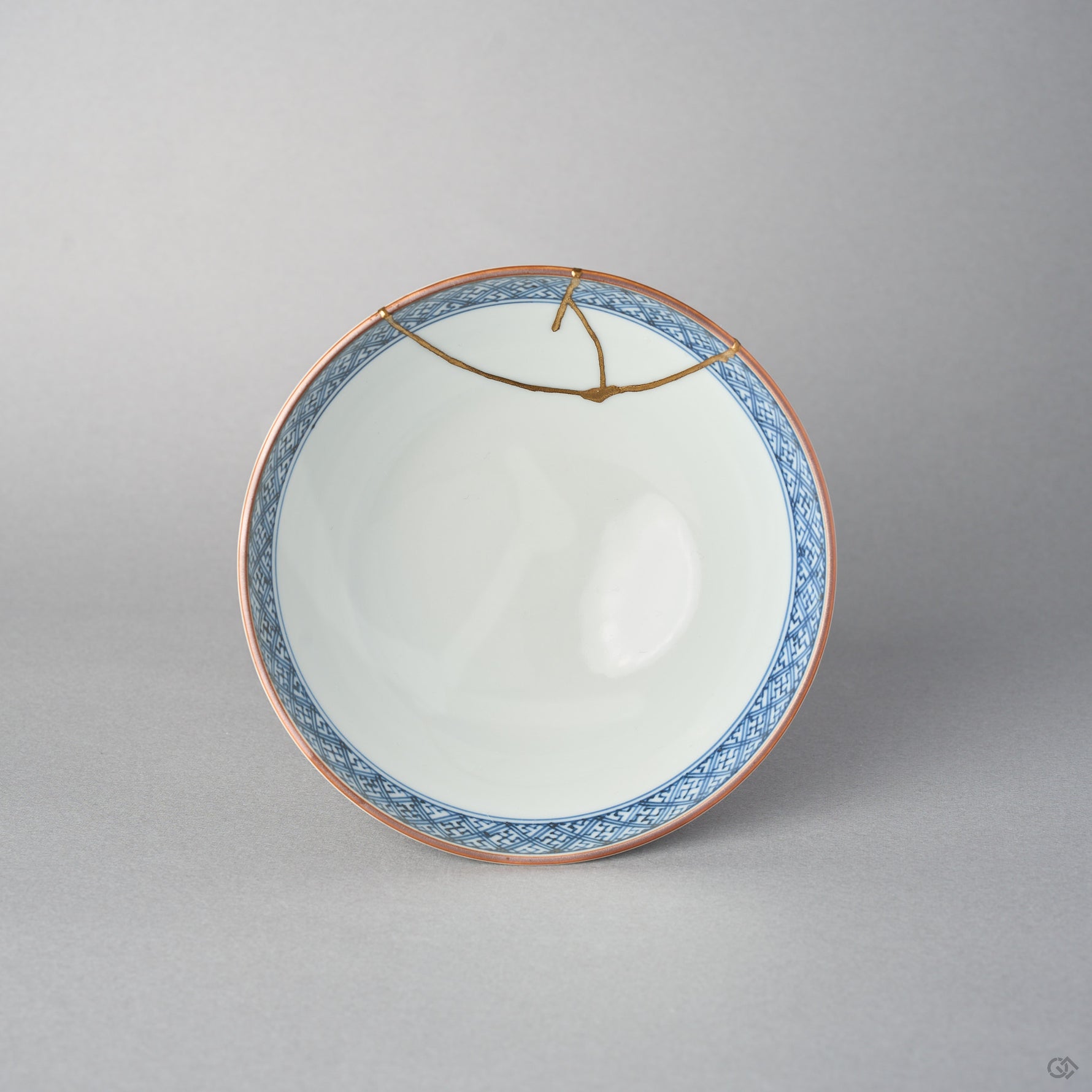 Top view of a kintsugi Kyoto ware rice bowl, the cobalt lattice border encircling a white porcelain well crossed by a branching 24K gold seam.