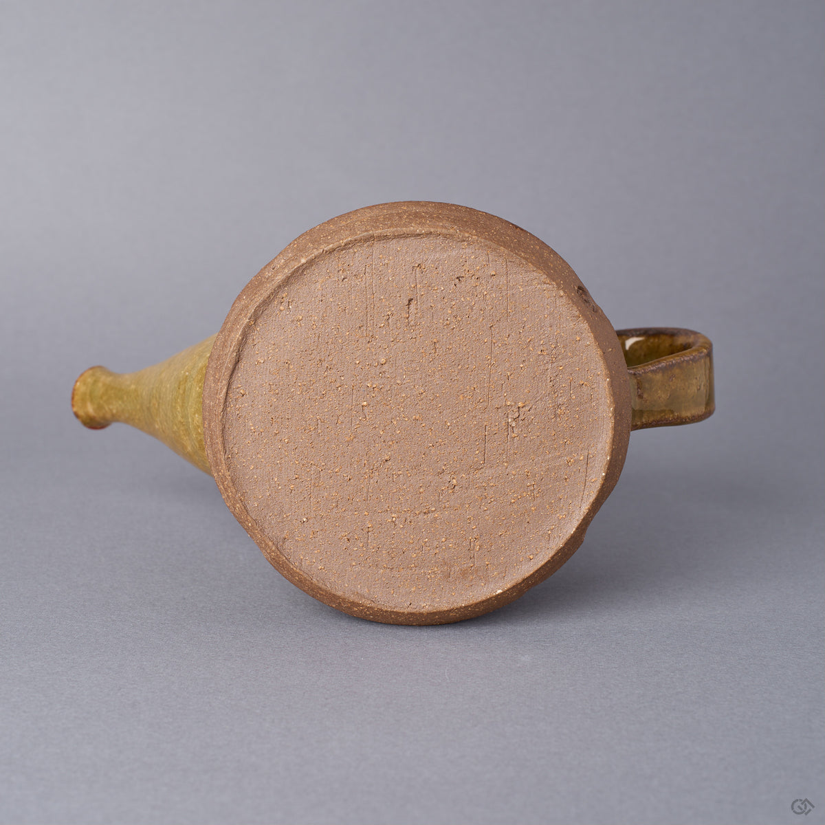 Bottom view of a Kyoto ware sake carafe showing the bare, warm-toned clay foot; no restoration on the base, ochre Oribe-green glaze rising at the body.