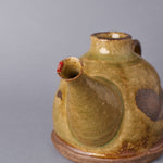 Close-up of the restored spout tip of a Kyoto ware sake carafe, a plum blossom in colored urushi outlined in 24K gold with pure-silver stamens, front view of the restoration.