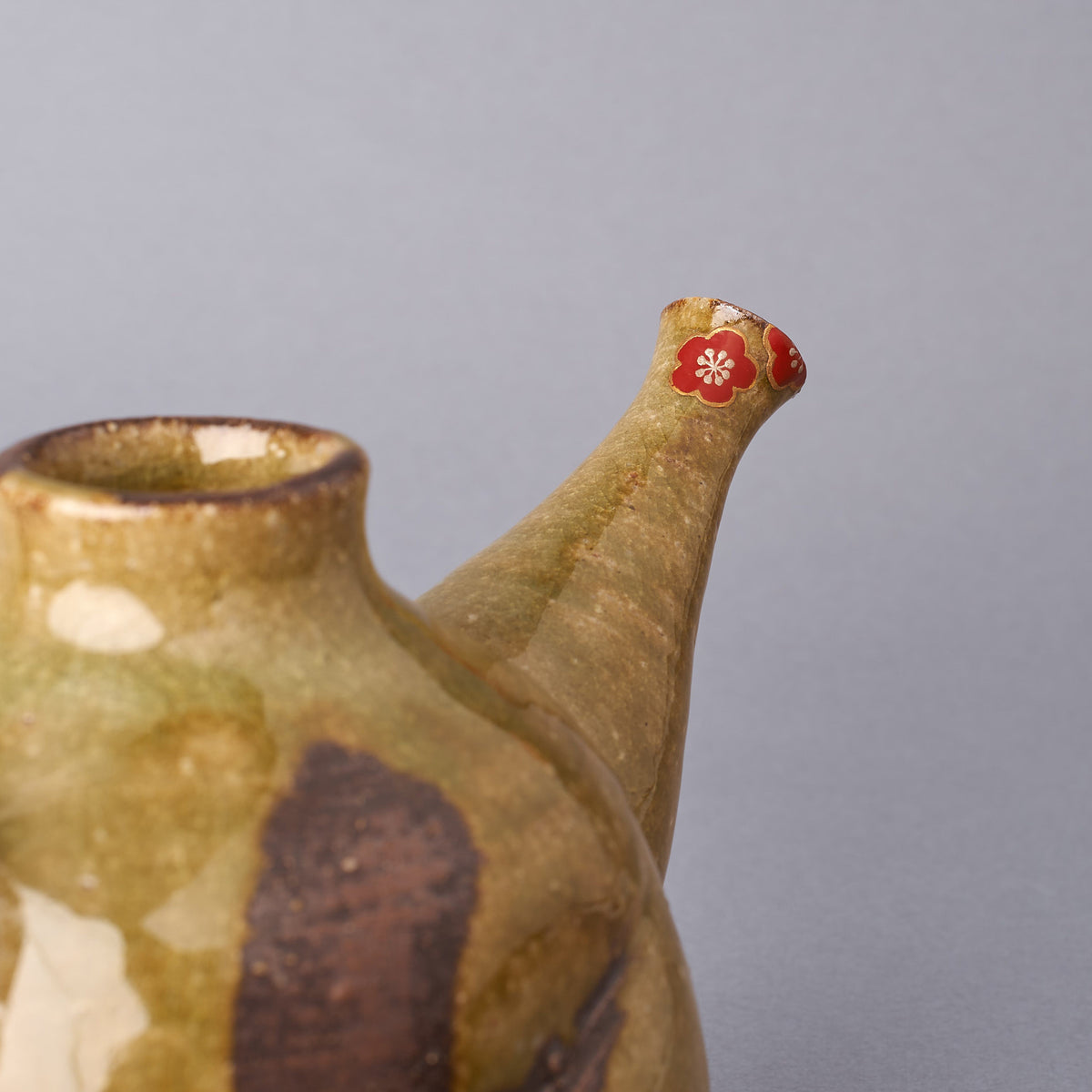 Side close-up of the plum-blossom restoration at the spout of a Kyoto ware sake carafe, colored urushi petals, 24K gold outline and silver heart over the chipped tip.