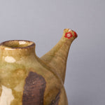 Side close-up of the plum-blossom restoration at the spout of a Kyoto ware sake carafe, colored urushi petals, 24K gold outline and silver heart over the chipped tip.